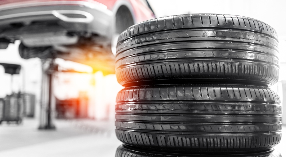 Image of stacked tyres and a vehicle lifted in an auto shop, representing premature tyre wear.